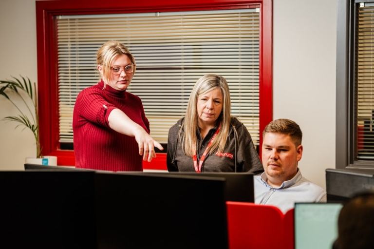 three people gathered around a computer screen talking