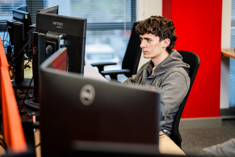 A Man Sat At His Desk Looking At His Computer Screen