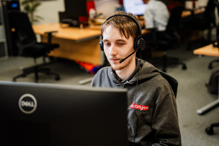 Man wearing a headset working at a computer, providing cyber security support using AI technology in an office environment.